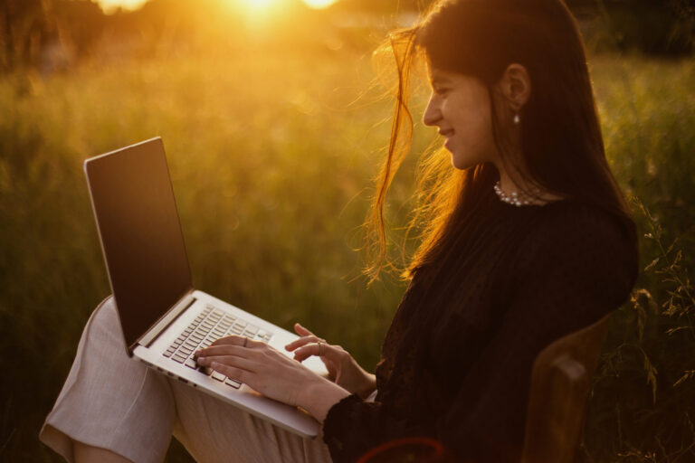 Frau arbeitet draußen mit Laptop bei Sonnenuntergang – Work-Life-Balance durch Workation.